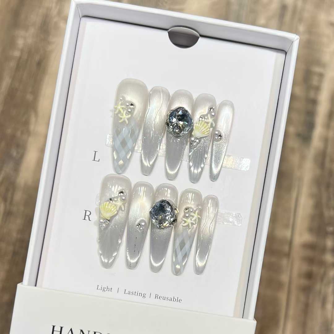 White and silver shell-motif press-on nails shown inside a white box